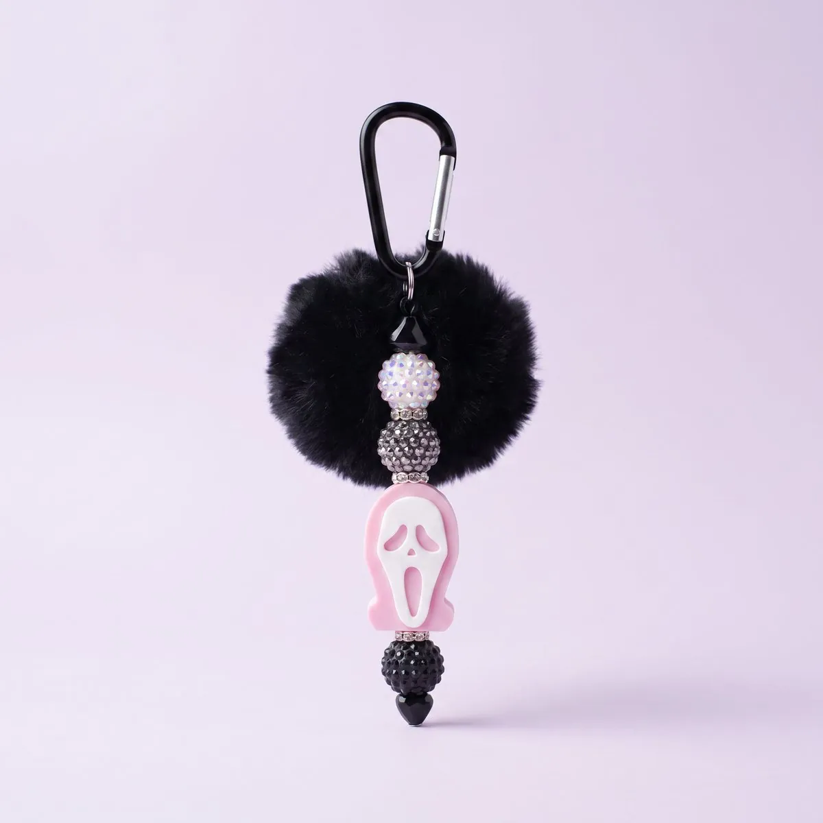 Blush Ghost Charm hanging from its black carabiner clip — a black faux-fur pom above a pale pink hooded ghost charm with a white face, strung with white iridescent, smoke-grey and black rhinestone beads and finished with a black heart bead
