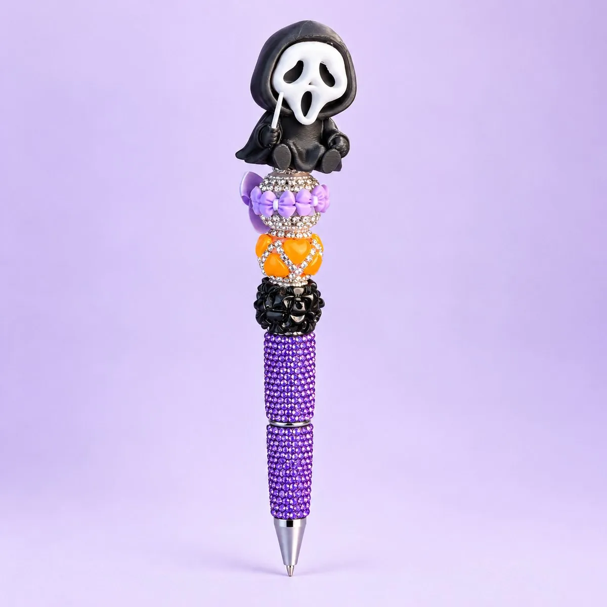Black Ghost Bling Pen on a pale lavender backdrop — pen with the black hooded white-masked ghost figure topper holding a knife, lilac bow bead, orange and black rhinestone beads, and a purple rhinestone barrel