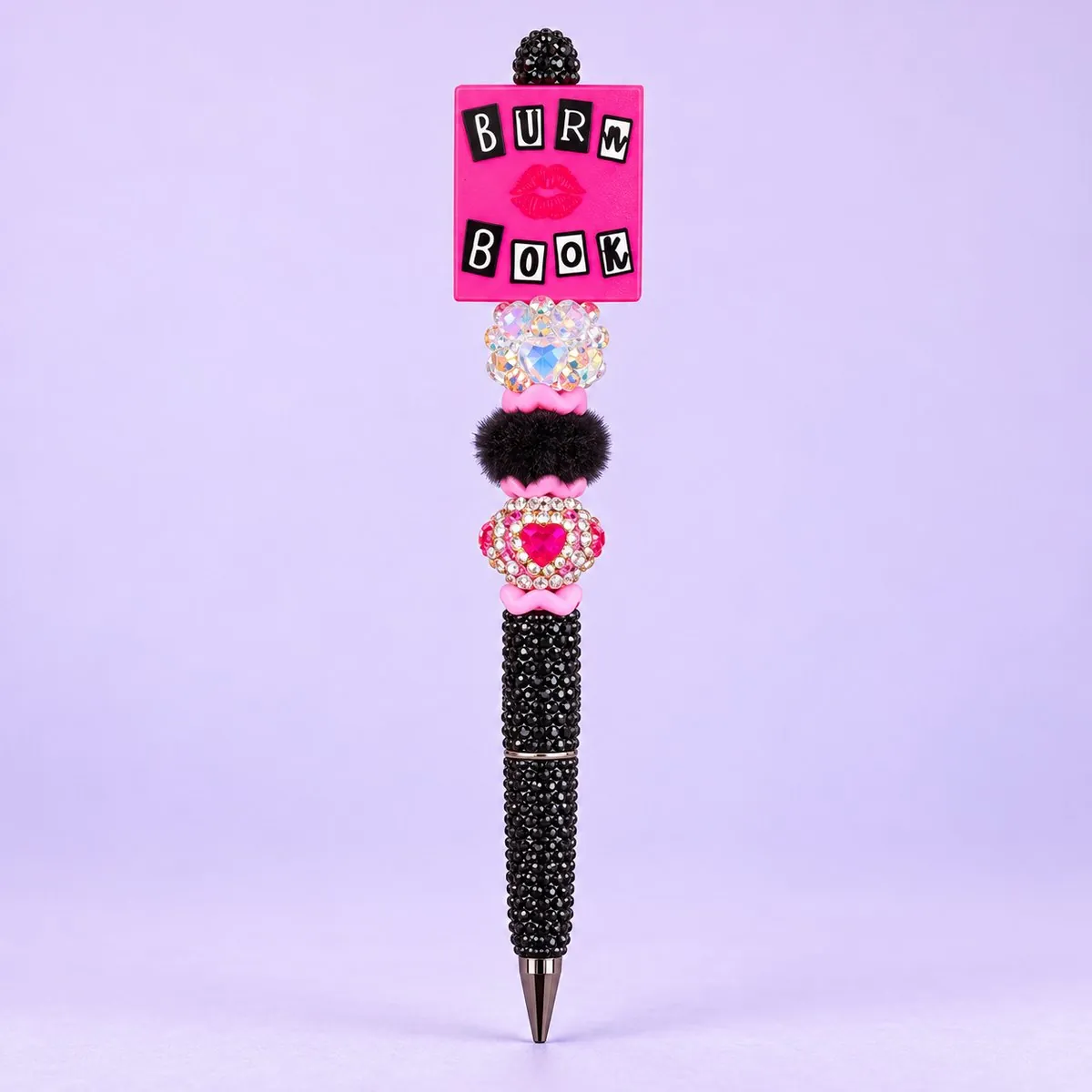 Burn Book Beaded Pen on a pale lavender backdrop — beaded pen with a hot-pink square 'BURN BOOK' book topper with a lip print, clear rhinestone, black fluffy and pink heart rhinestone beads, and a black rhinestone barrel