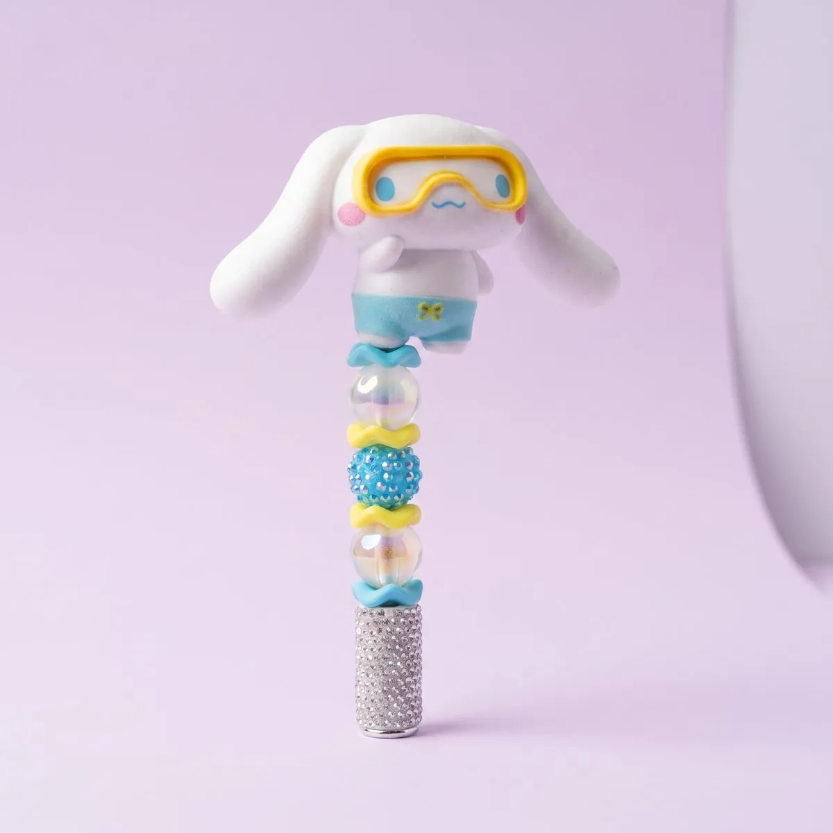 Puppy Snorkeler Beaded Pen standing upright — a silver rhinestone barrel strung with iridescent bubble beads, yellow wavy spacers and an aqua rhinestone bead, topped with a long-eared white puppy in a yellow snorkel mask and blue swim shorts