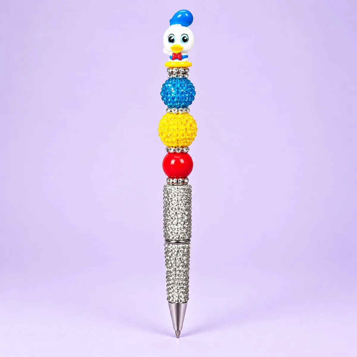 Sailor Duck Beaded Pen on a pale lavender backdrop — beaded pen with a white duck in a blue sailor hat topper, blue, yellow and red beads, and a silver rhinestone barrel