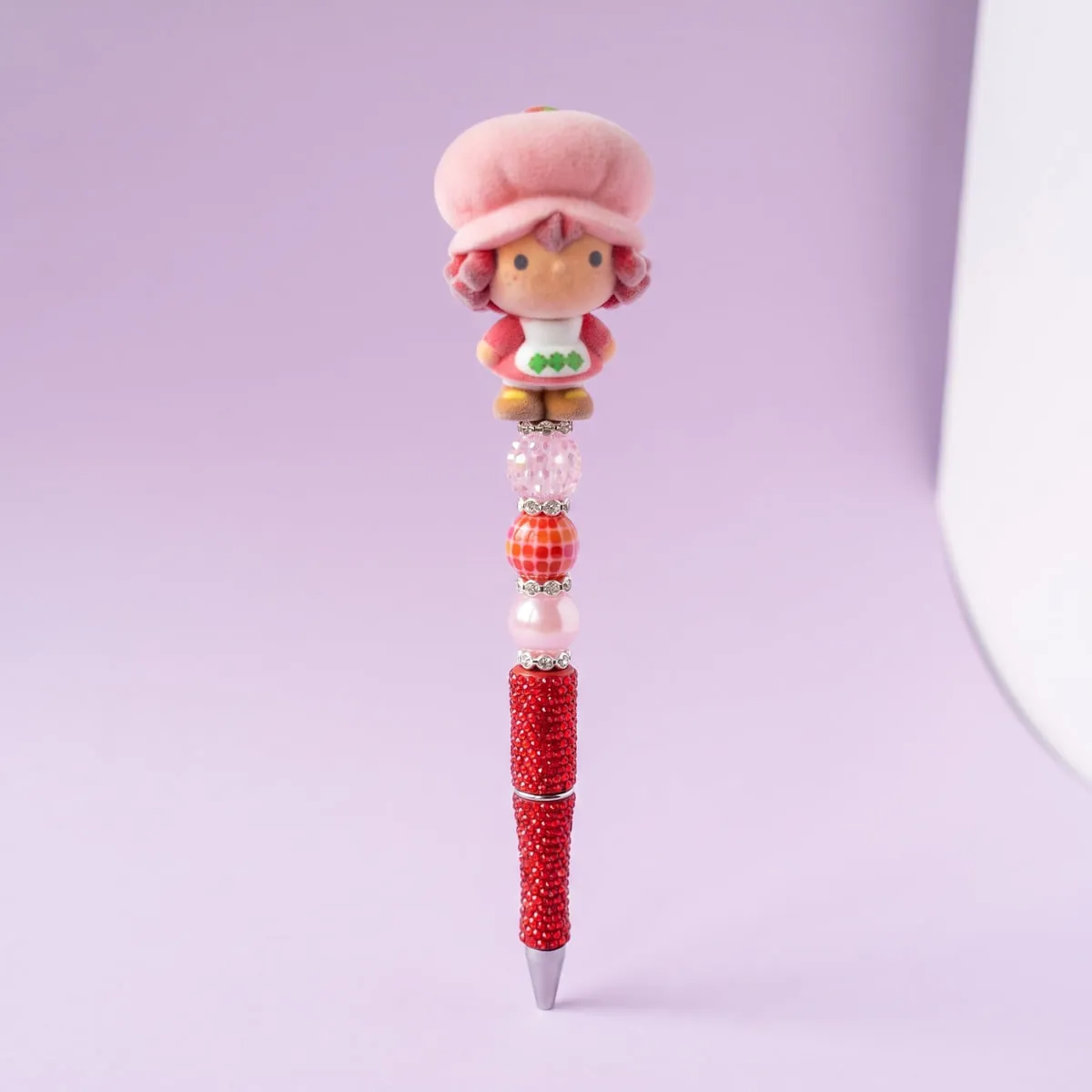 Strawberry Sweetie Beaded Pen standing upright — a red rhinestone barrel strung with pink, red and crystal beads beneath a berry-girl doll topper in a pink bonnet