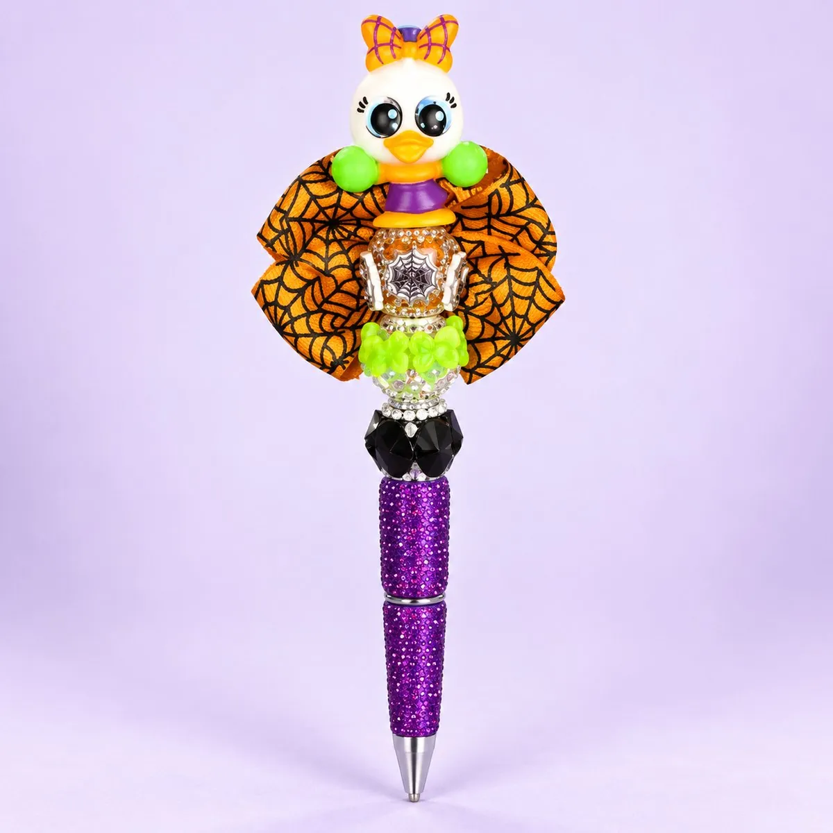 Witchy Duck Beaded Pen on a pale lavender backdrop — beaded pen with a white duck girl topper with an orange bow, a large orange-and-black spiderweb ribbon bow, lime and black beads, and a purple glitter barrel