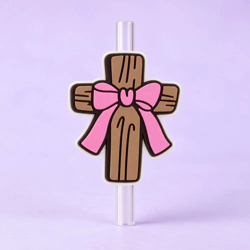 Bow Cross Topper on a clear straw, pale lavender backdrop — shaped like a brown wooden-look cross with a pink ribbon bow
