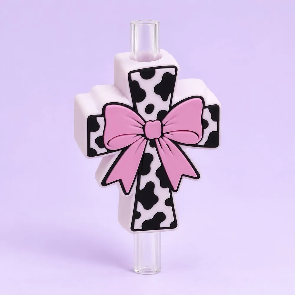 Cow Print Cross Topper on a clear straw, pale lavender backdrop — shaped like a white cow-print cross with a pink bow